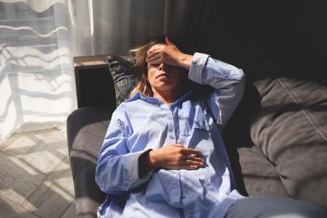 Woman lying on a couch, hand on forehead, appearing stressed.