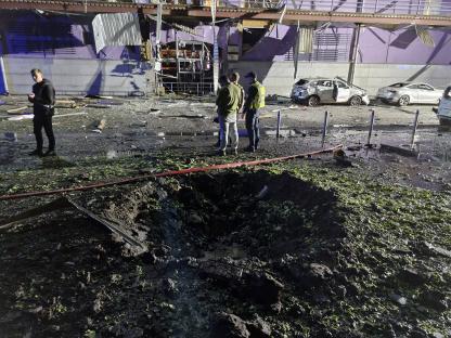 Municipal workers cleaning near burnt cars and a crater in Kyiv, Ukraine.