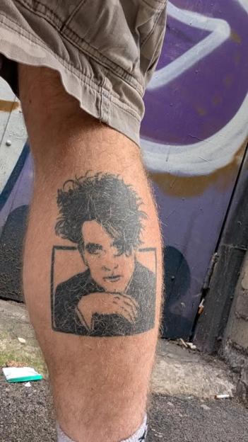 Tattoo of a portrait of Robert Smith on a person's leg.
