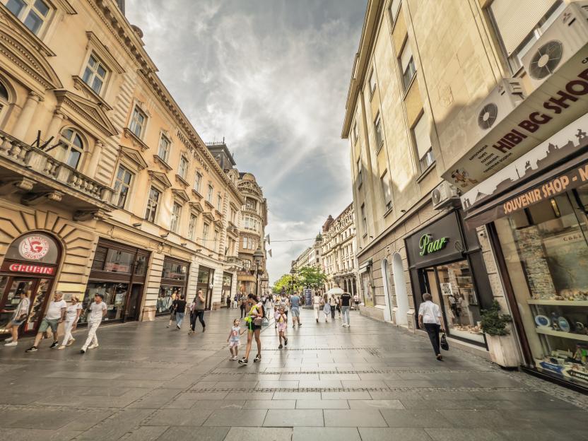 Kneza Mihailova Street in Belgrade, Serbia, bustling with pedestrians walking past historic 19th and early 20th-century buildings housing shops, souvenir stores, and cafes.