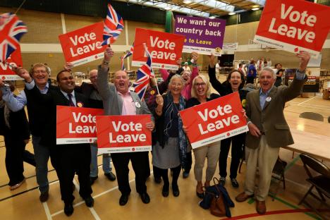 People holding Vote Leave signs at a referendum count.