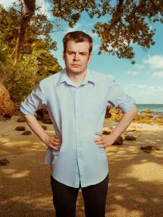A man standing on a beach with his hands on his hips, looking unhappy.