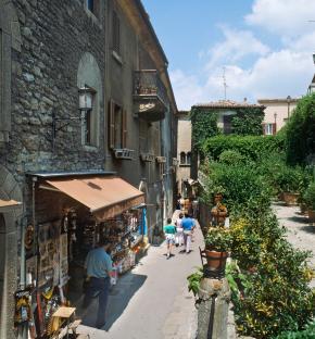 Tourists walking down a narrow street in San Marino, Italy, lined with stone buildings and shops.