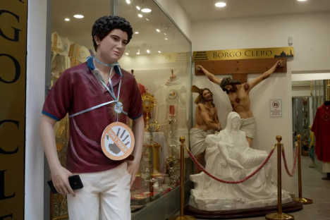 Statue of a young man with a "Don't Touch" sign, displayed in a shop window with religious statues.