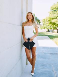 Graduate in white dress holding graduation cap.