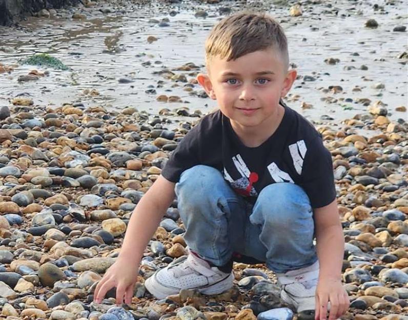 Young boy crouching on a pebbled beach.