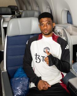 Amad Diallo of Manchester United gives a thumbs-up while seated on an airplane.