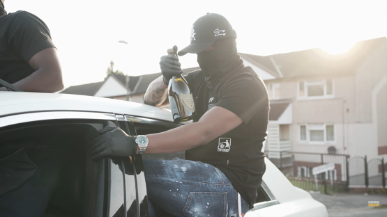 Man holding champagne bottle by a car.