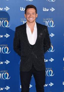 a man in a sequined jacket stands in front of a blue wall that says itv