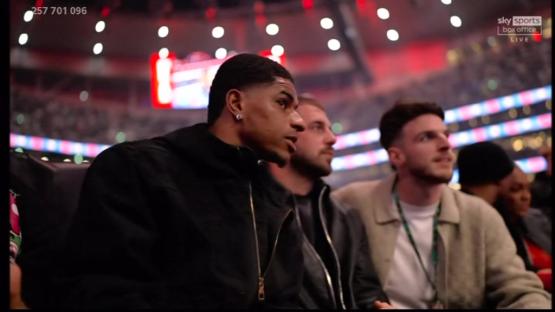 A man sits among a crowd at a boxing match.