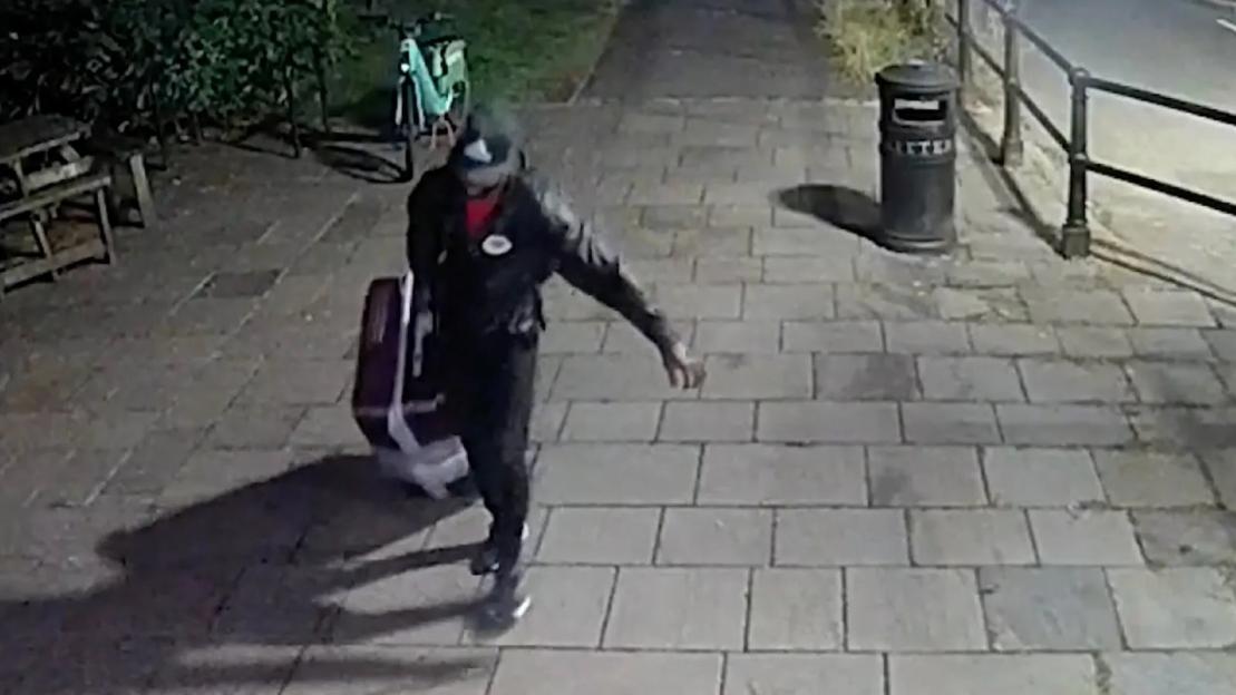 A man dragging a large suitcase down a paved path at night.