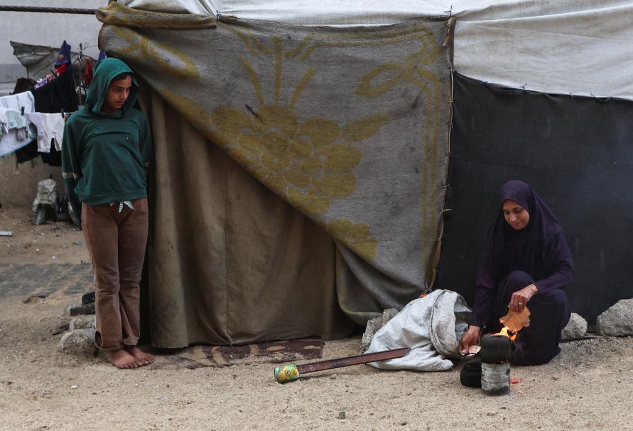 A Palestinian woman builds a fire as a girl watches from beside a tent in Khan Younis, southern Gaza Strip.