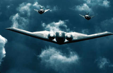 B-2 Spirit bomber with two fighter jets flying above clouds.