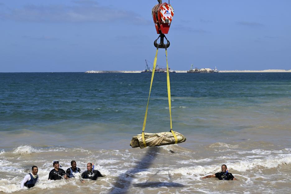 Divers watch as a crane lifts an artifact from the water.