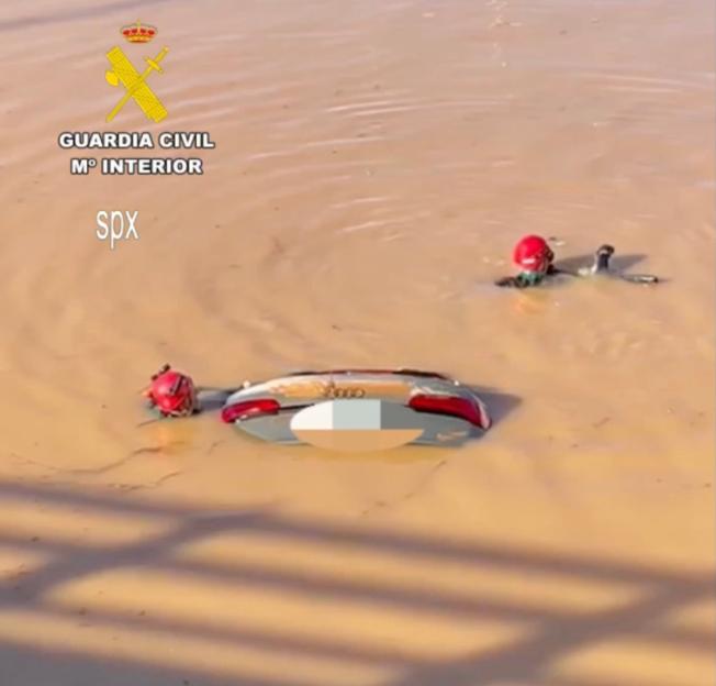 Submerged vehicle with the back half and two red helmets visible in murky floodwaters.