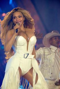 Beyoncé performing on stage in a white fringed outfit.