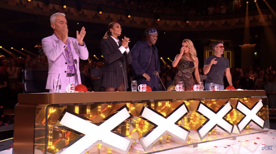 Screenshot of four judges at the judges' table of a talent show, reacting to a performance.