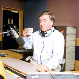 Terry Wogan, radio and TV star, holding a mug in a recording studio.