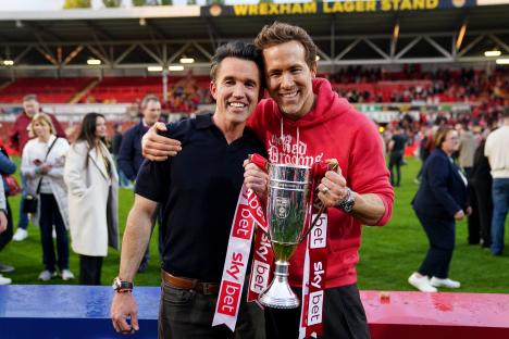 Rob McElhenney and Ryan Reynolds celebrating with a trophy.