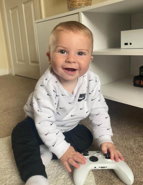 A toddler in a Nike sweatshirt holds an Xbox controller.