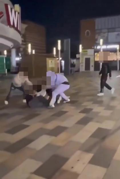 Four blurred figures in a street brawl, one on the ground being attacked by two others.