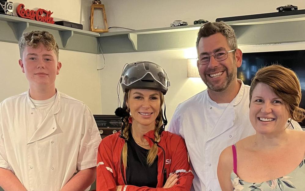 Group photo of four people, two in chef's whites, one in a cycling helmet and red jacket, and one in a floral dress.