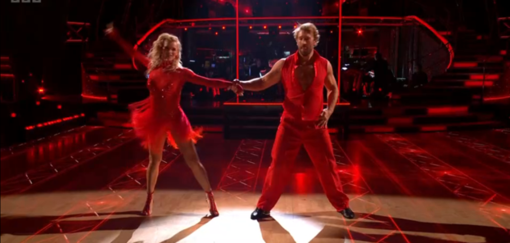 Two dancers in red outfits performing on a stage with red lighting.