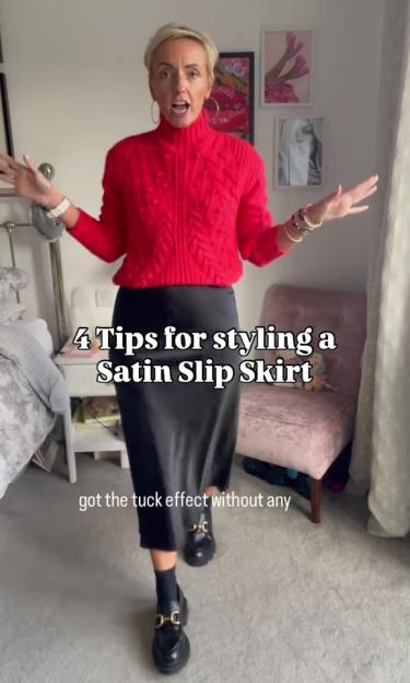 A woman in a red sweater and black satin slip skirt giving tips on styling the skirt.