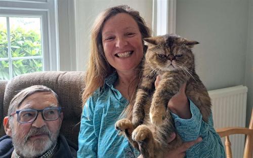 Woman holding a cat, with an older man seated beside them.