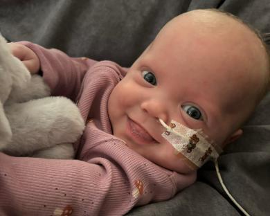 Smiling baby girl in pink outfit with nasal cannula.