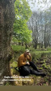 David Beckham sitting on the ground in a wooded area.