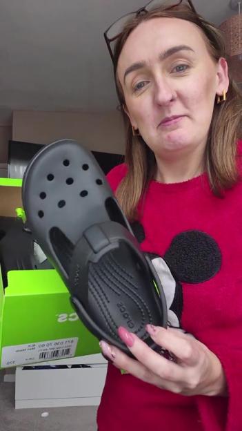 Woman holding up a black Croc shoe.