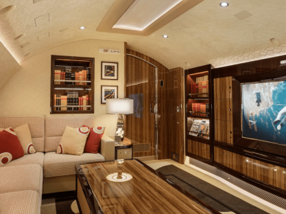 Luxury private jet lounge with seating area, bookshelves, and large screen TV.