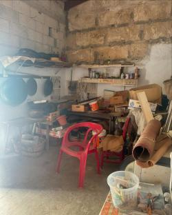 Cluttered storage room with stone walls, shelves, and various items.