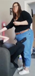 Woman holding a small bottle, standing next to a person sitting on a couch.