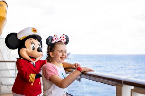 A girl in Minnie Mouse ears stands at a ship railing with a costumed Minnie Mouse.