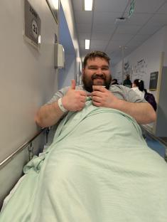 Man in hospital bed giving thumbs up.