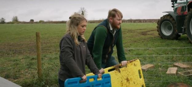 Two people carrying muddy carrying boards in a field.