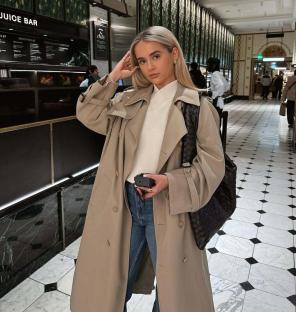 Woman in beige trench coat and jeans in a building.