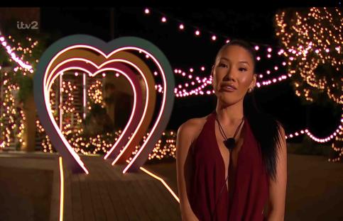 Woman in red dress standing before a heart-shaped light display.