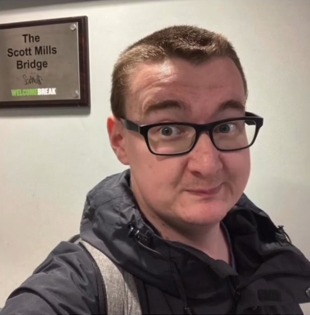 Rich James Cross, "The Service Station King", in front of "The Scott Mills Bridge" sign.