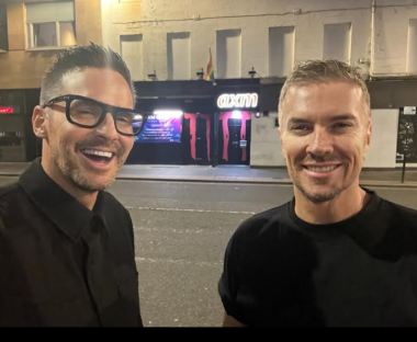 Two men smiling in front of Axm nightclub.