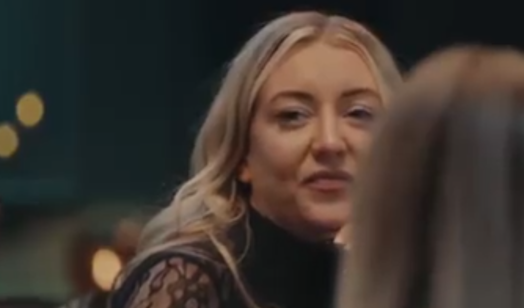 A blonde woman with dark eyeliner and eye shadow looks to her right.
