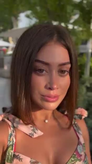 A woman in a floral top and pearl necklace looks directly at the camera.