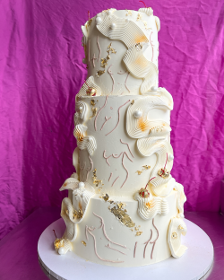 Three-tiered wedding cake decorated with gold leaf and cherries.