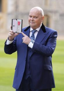 James Whale holding his MBE medal after an investiture ceremony at Windsor Castle.