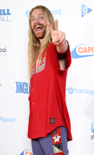 Man with long blond hair making peace sign at an event.