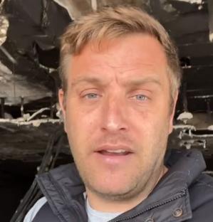 Man speaks in front of fire-damaged restaurant.