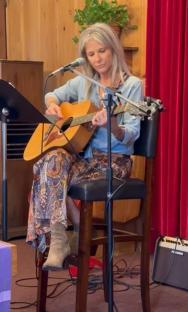 Woman playing acoustic guitar on stage.