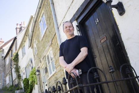A man stands outside a cottage on Gold Hill in Shaftesbury, England.